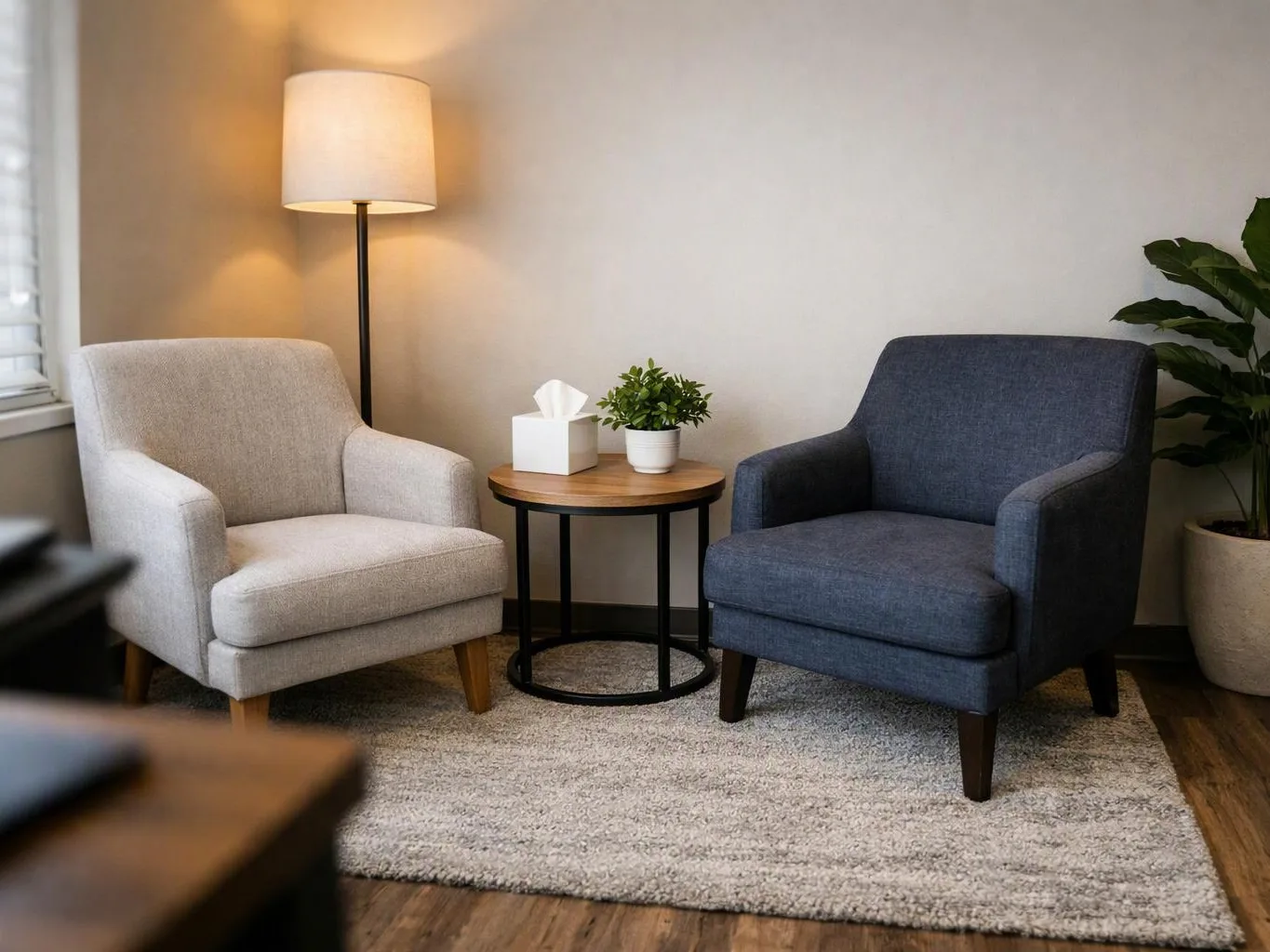 Two armchairs sit beside a round side table and floor lamp in a cozy living room nook